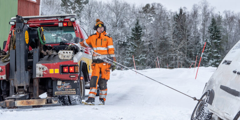 Bärgare från Assistancekåren Skövde vinschar loss en bil som kört av vägen på en snötäckt landsväg.