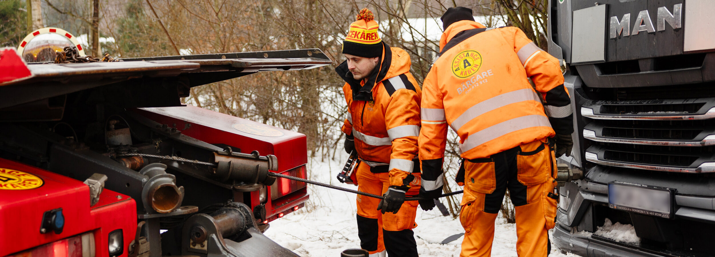 Bärgare från Assistancekåren i Sjöbo kopplar vinschvajer vid bärgning av lastbil på vinterväg.