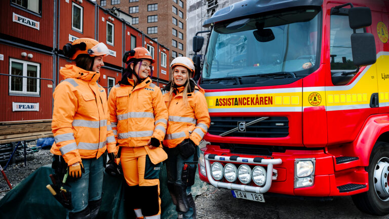 Tre medarbetare från PEAB står framför en bärgningsbil från Assistancekåren vid en byggarbetsplats. Bilden illustrerar det nya rikstäckande samarbetet mellan Assistancekåren och PEAB.